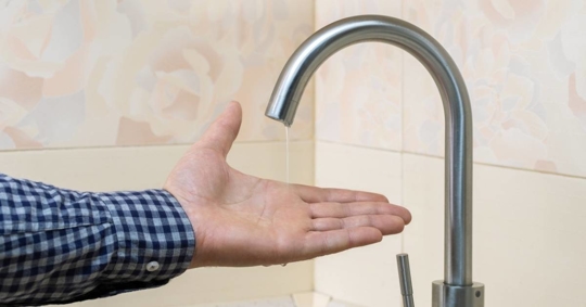 Male hand and faucet with water pouring in a thin steady stream.