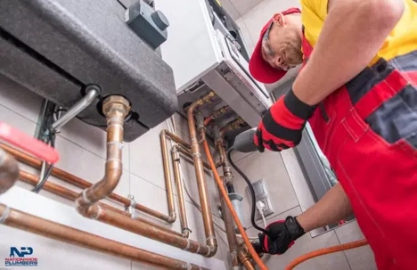A plumber is working on the pipes connected to a wall-mounted boiler.