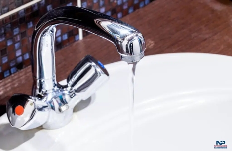 A faucet mounted over a white sink with water running.