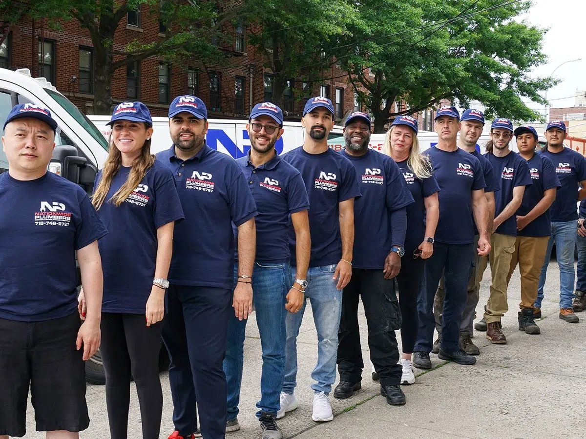 A team of plumbers, wearing branded shirts and hats, stand in a line in front of their work van.